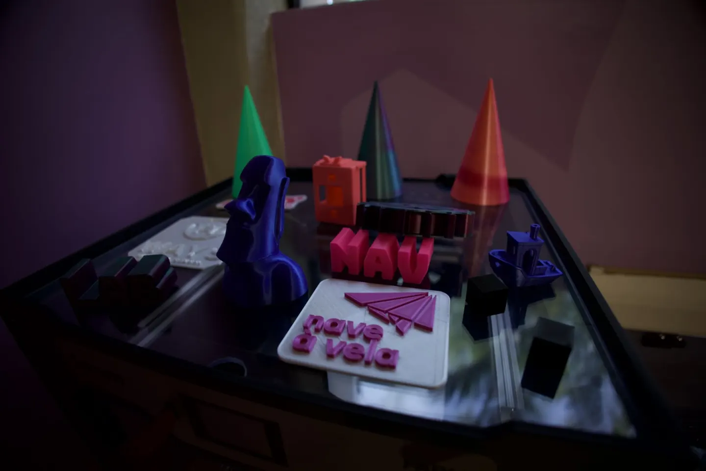 Peças coloridas feitas em impressora 3D, como um barquinho, cones e uma estátua moai