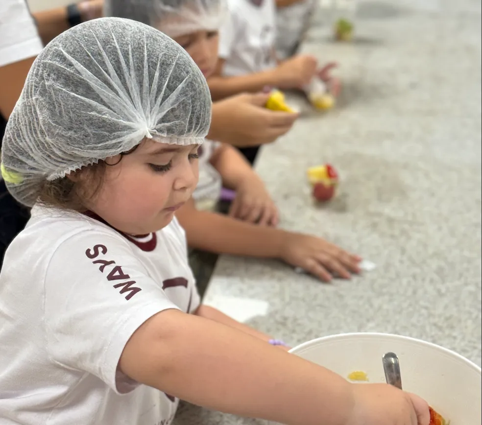 Crianças de touca preparando salada de frutas numa bancada
